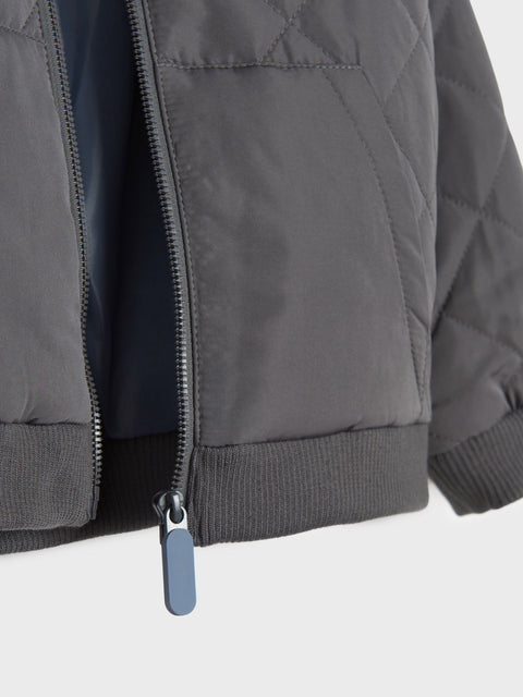 Close-up of a dark gray quilted jacket with a zipper on a white background