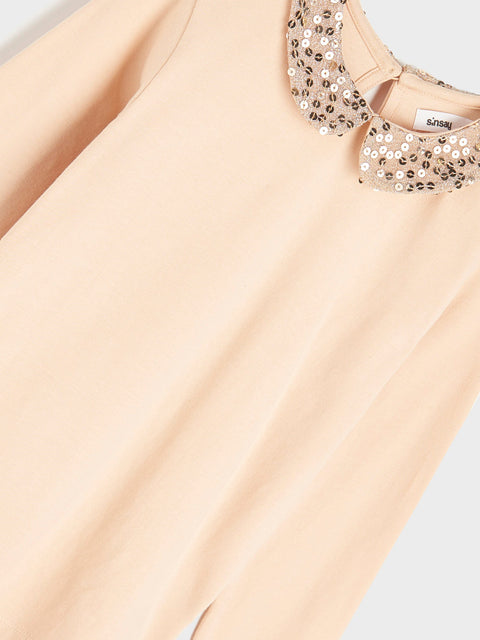 Beige top with sequin embellishments on a light gray background