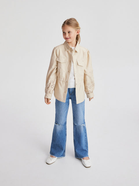 Young girl wearing a beige jacket and blue jeans on a white background