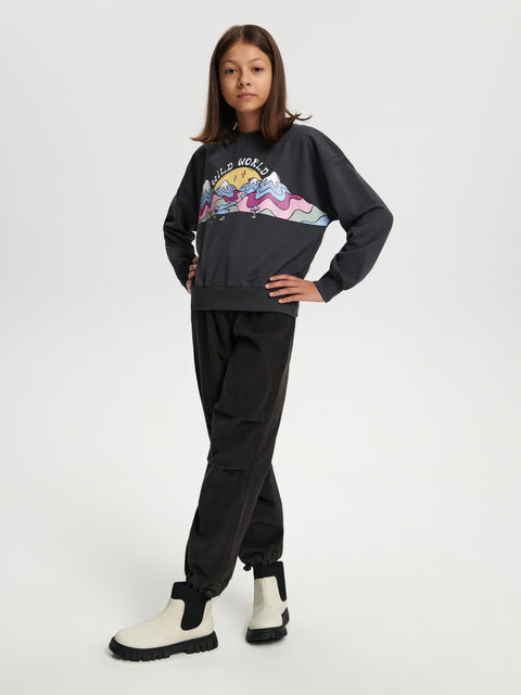 Person wearing a black hoodie with a colorful graphic and black pants on a white background