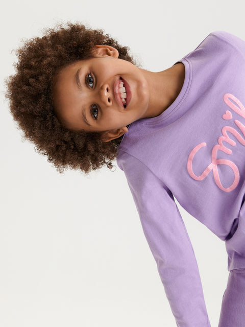 Child wearing a purple sweatshirt with 'Smile' written on it against a white background