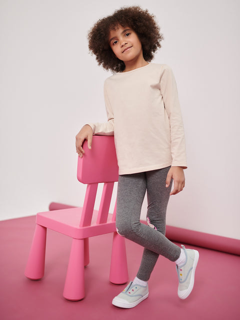 Child standing next to a pink chair on a pink floor with a white background