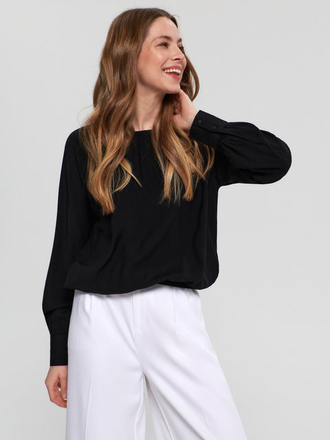 Woman wearing a black top and white pants against a plain background