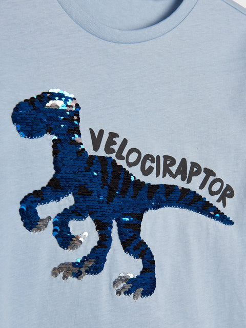 Light blue t-shirt with sequin velociraptor design and 'VELOCIRAPTOR' text on a light gray background