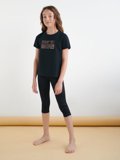 Young girl wearing a black t-shirt and leggings on a plain background