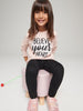 Young girl sitting on a pink stool wearing a pink shirt with 'BELIEVE YOUR HEART' text.