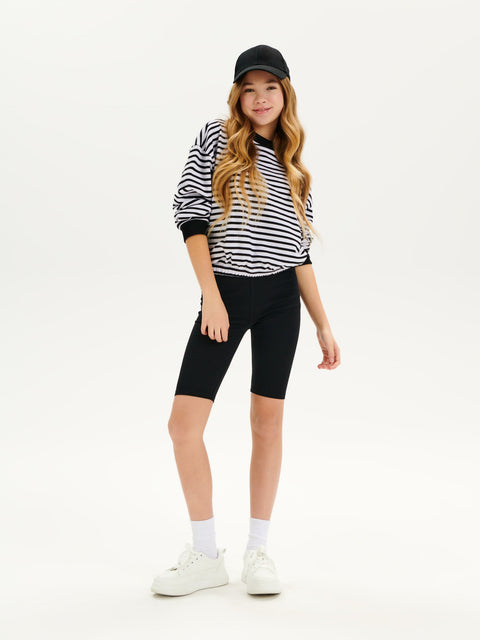 Person wearing a black and white striped shirt, black capri pants, and white sneakers on a white background
