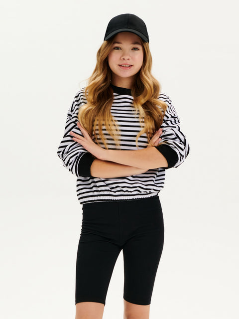 Person wearing a black and white striped sweater with black capri pants on a white background