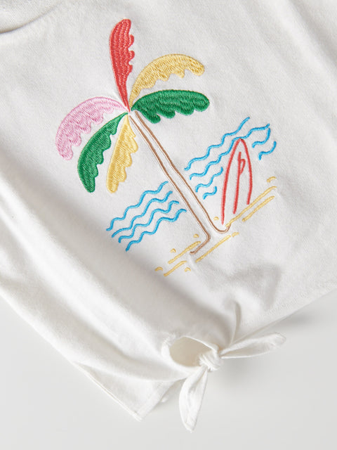 Embroidered design of a palm tree and surfboard on a white fabric with a knot.