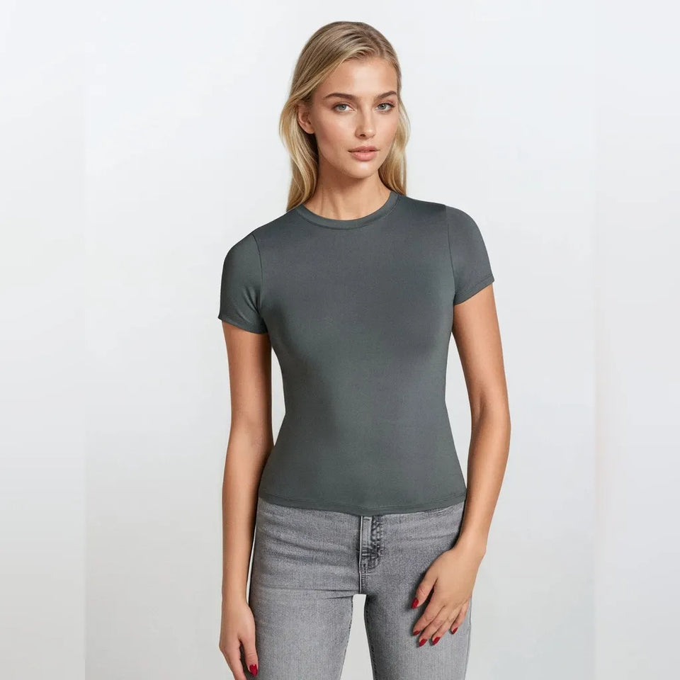A woman modeling a fitted short-sleeve crewneck t-shirt in dark gray, paired with light gray jeans, against a plain white studio background.