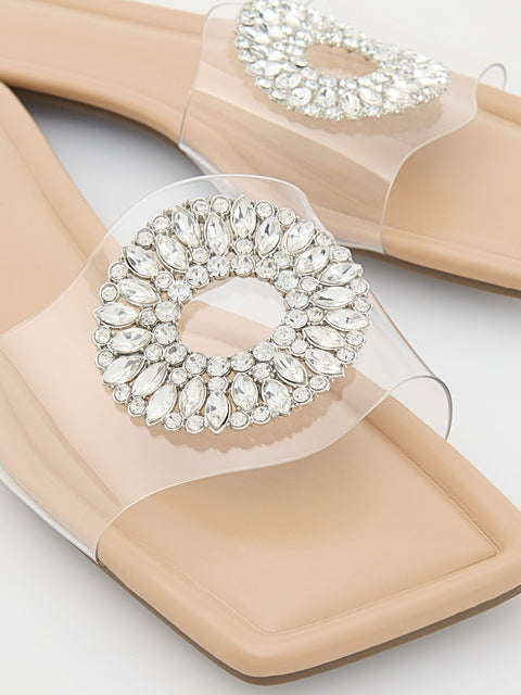 Beige sandals with clear straps and large crystal embellishments on a light background