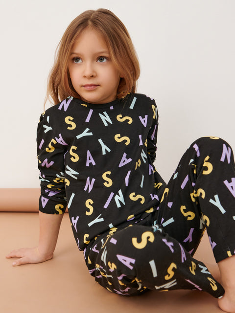 Child wearing a black outfit with colorful letters on a beige background