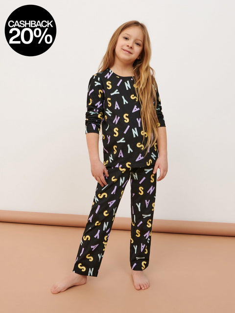 Young girl wearing a black pajama set with colorful letter patterns on a beige background