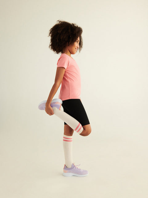 Child wearing a pink shirt, black shorts, and white knee-high socks with pink stripes on a light background