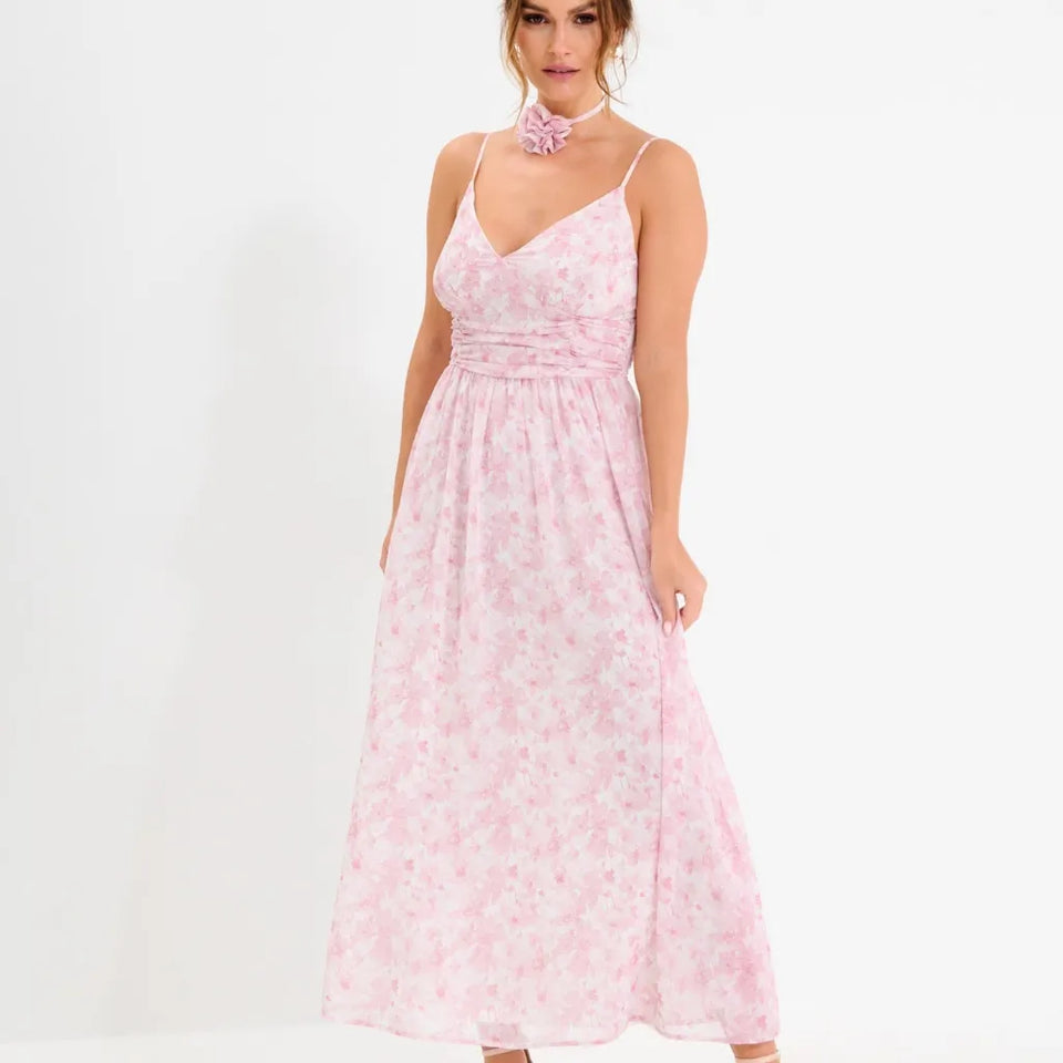 A woman modeling a light pink sleeveless maxi dress with a delicate floral pattern, featuring thin spaghetti straps, a V-neckline, and a gathered waist.