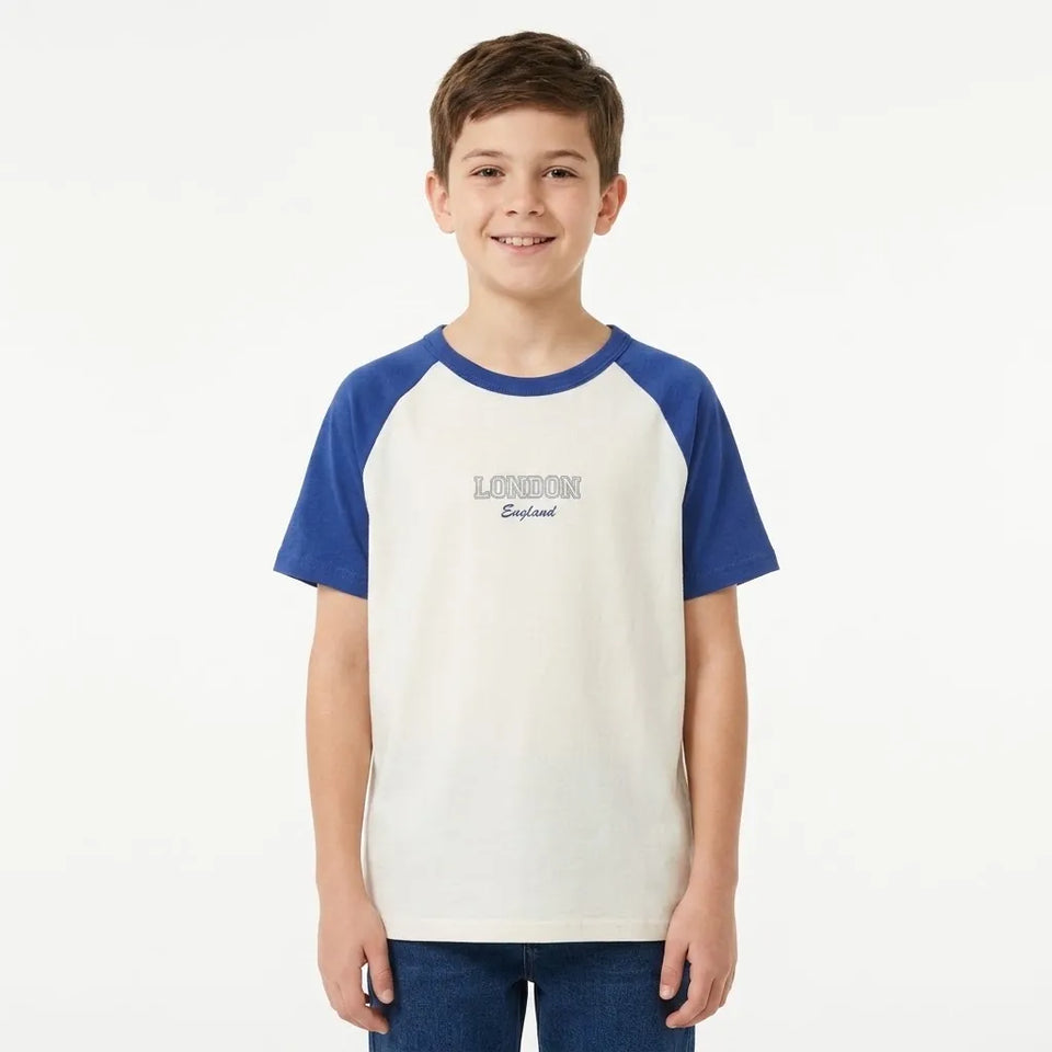A young boy wearing a raglan-style t-shirt with a cream body and blue sleeves, featuring 'LONDON England' printed on the chest, set against a plain white background.