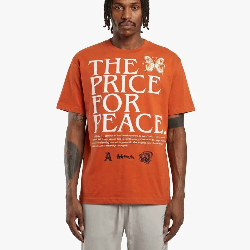 A man wearing a bright orange t-shirt with 'THE PRICE FOR PEACE' printed in large white letters, featuring a butterfly graphic and text on the front, paired with light gray pants, against a plain light gray background.