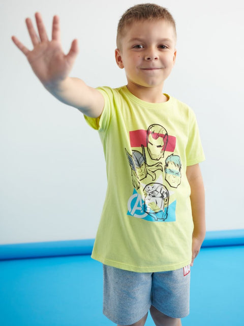 A boy wearing a yellow short-sleeve t-shirt with a graphic design, standing with one hand raised.