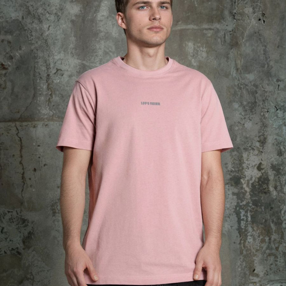 A man wearing a light pink crewneck t-shirt with a small 'UPPY TRUCK' logo on the chest, standing against a textured gray concrete wall.