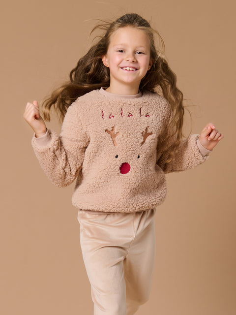 Young girl wearing a fluffy sweater with reindeer design and 'Santa' text on a beige background