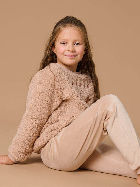 Young girl wearing a cozy beige sweater and pants sitting on a beige background
