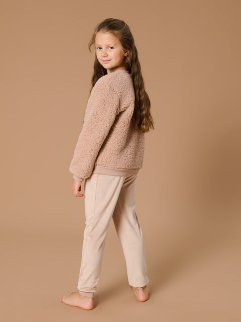 Young girl wearing a beige fluffy sweater and pants on a brown background