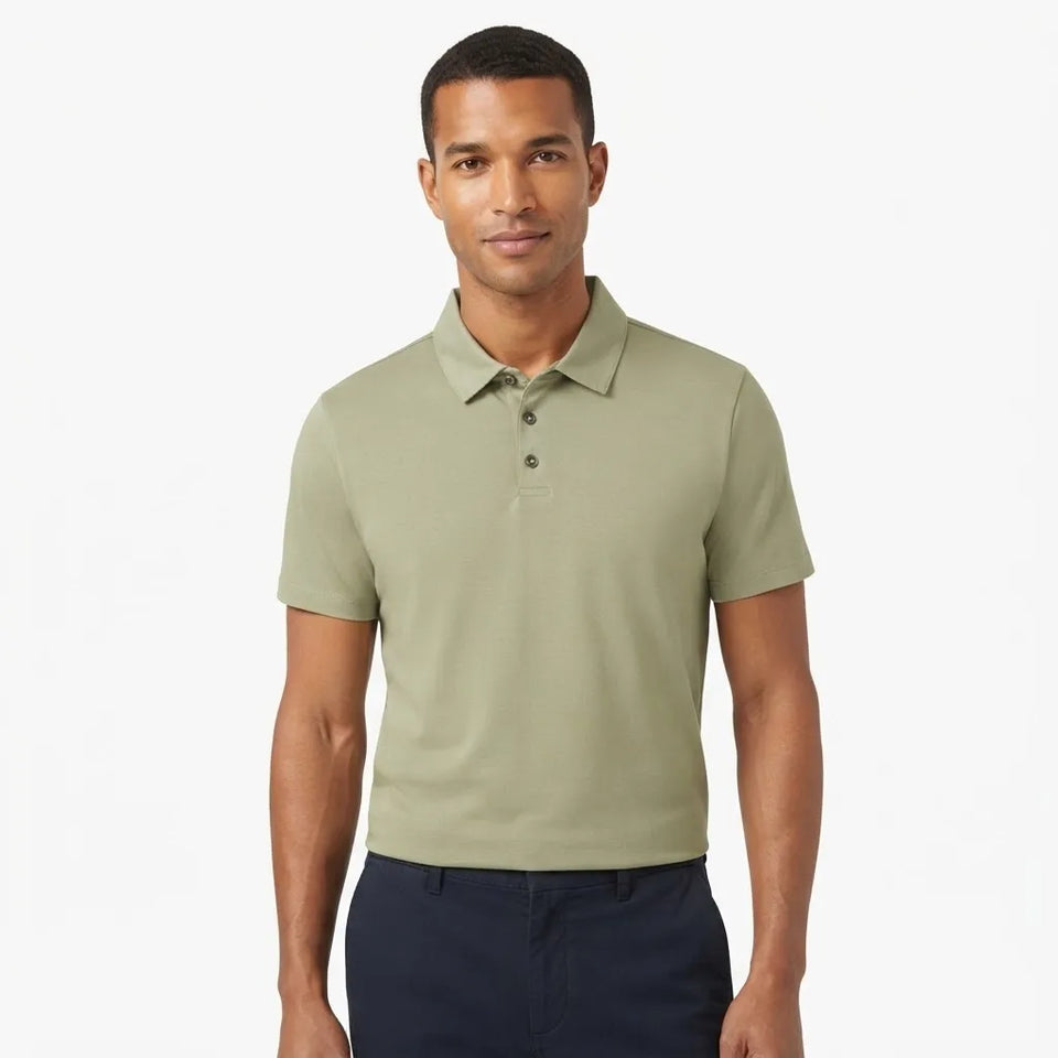 A man wearing a short-sleeve polo shirt in sage green, paired with dark navy pants, standing against a plain white studio background.