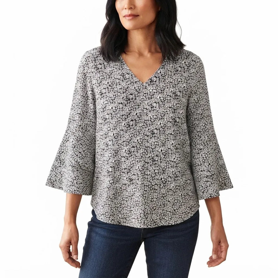 A woman wearing a black and white floral print blouse with three-quarter bell sleeves and a V-neckline, paired with dark blue jeans, against a plain white background.