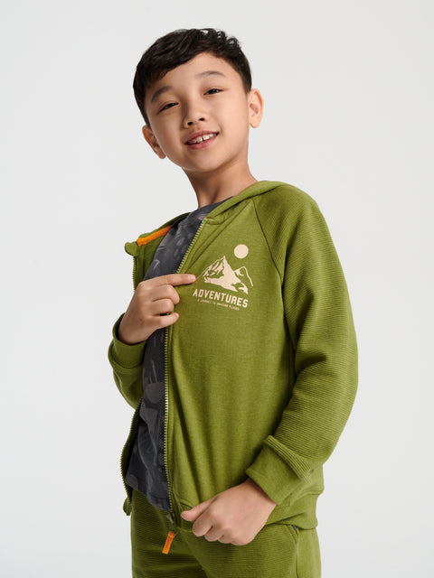 Child wearing a green hoodie with 'Adventures' logo on a white background