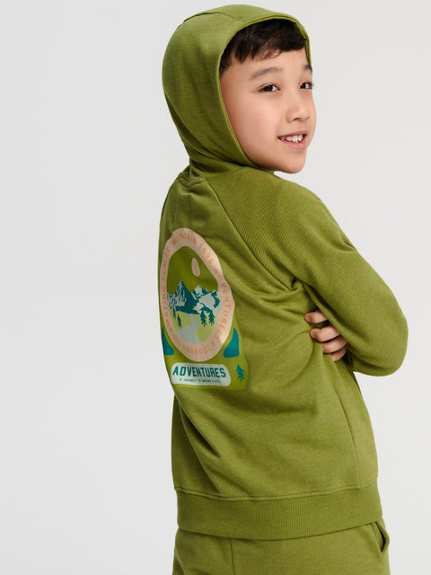 Child wearing a green hoodie with a 'Adventures' patch on a white background