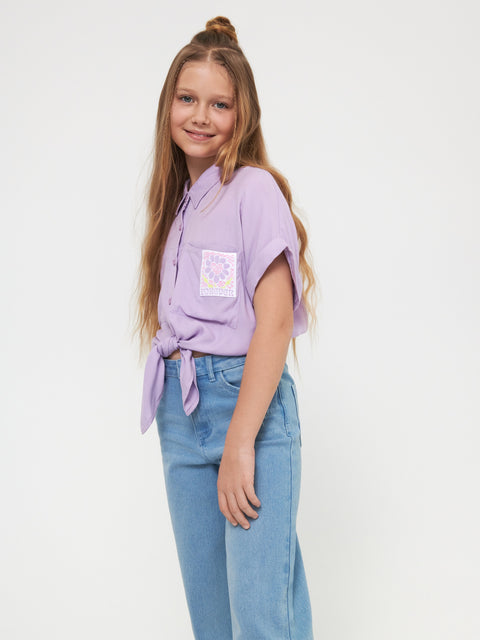 Young girl wearing a purple shirt with a pocket and blue jeans on a white background