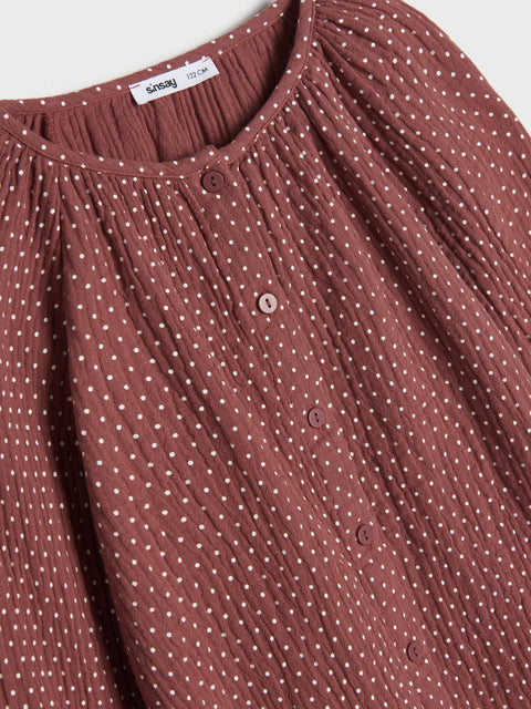 Close-up of a brown polka dot shirt with a brand label on a white background