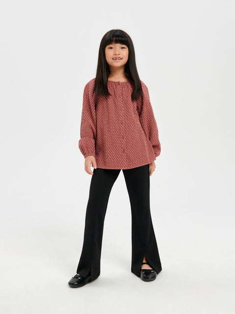 Young girl wearing a pink textured sweater and black pants on a white background
