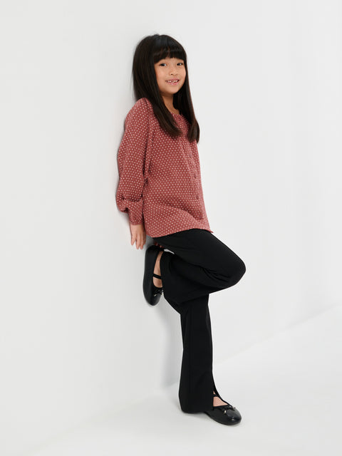 Young girl wearing a pink sweater and black pants on a white background