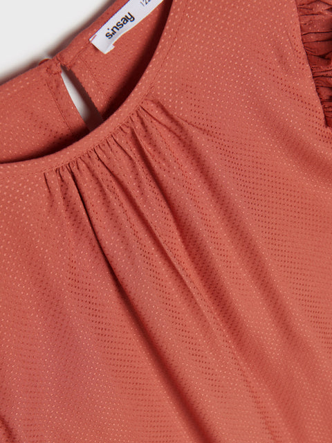 Close-up of a rust-colored blouse with a brand label on a white background