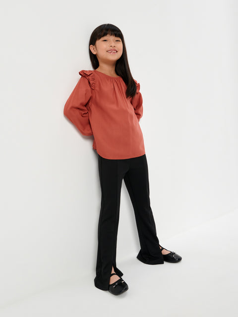 Young girl wearing a rust-colored blouse and black pants on a white background