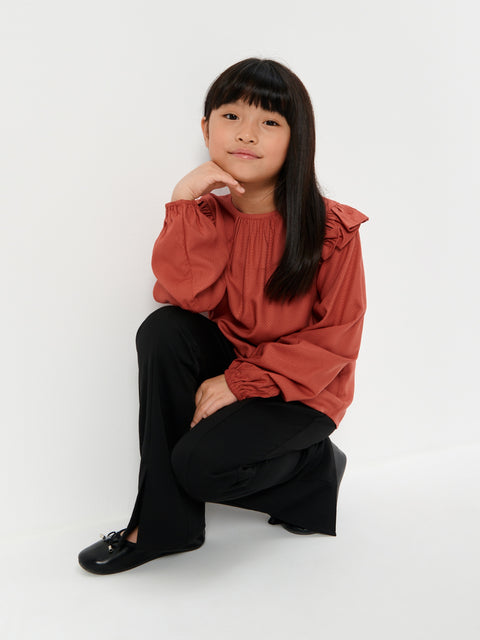 Person wearing a rust-colored blouse and black pants on a white background