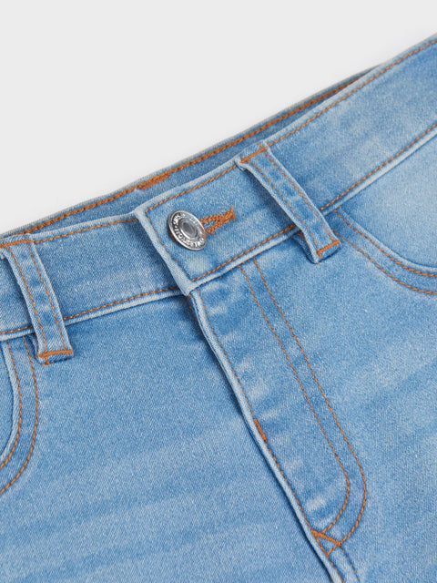 Close-up of a blue denim pocket with button and stitching detail on a light gray background
