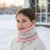 A young girl wearing a pink and gray patterned knit neck warmer in a snowy outdoor setting.