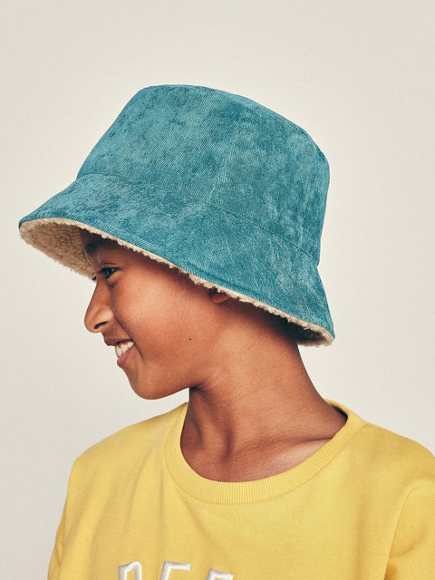Person wearing a blue bucket hat with beige interior and a yellow shirt on a plain background