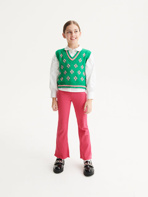 Person wearing a green patterned sweater over a white shirt with pink pants on a white background