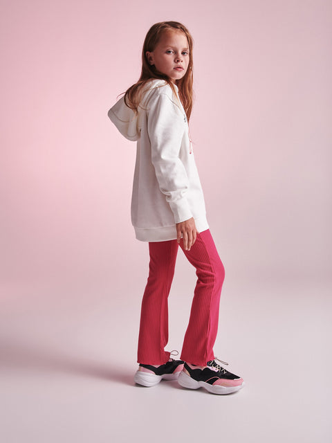 Young girl wearing a white hoodie and pink pants on a light pink background