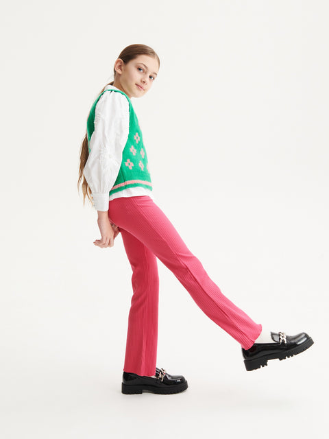 Person wearing a green and white sweater with floral patterns, pink pants, and black shoes on a white background