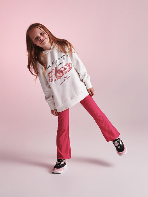 Young girl wearing a white hoodie with pink text and pink pants on a pink background