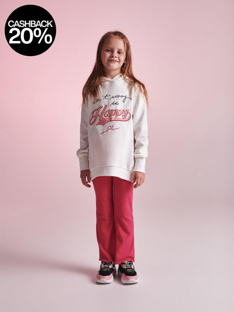 Young girl wearing a white hoodie with text and red pants on a pink background