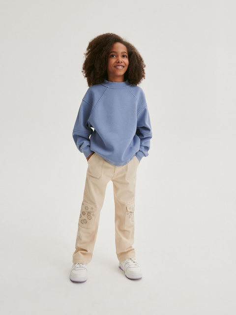 Child wearing a blue sweatshirt and beige pants on a white background