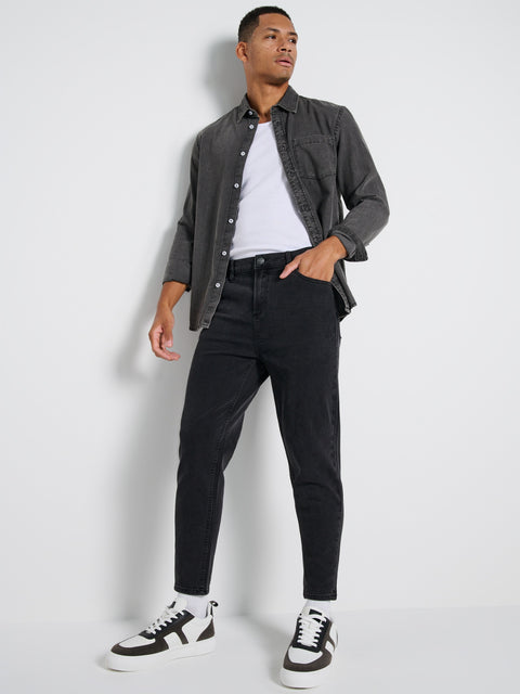 Man wearing a gray shirt, white t-shirt, black jeans, and black and white sneakers on a light gray background