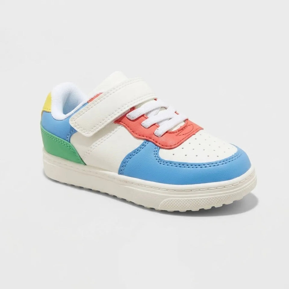 A toddler's white low-top sneaker with colorful accents in light blue, coral red, green, and yellow, featuring a hook-and-loop strap closure and white laces, shown on a light gray background.