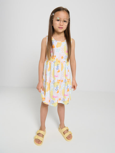 Young girl wearing a patterned dress and yellow sandals on a white background