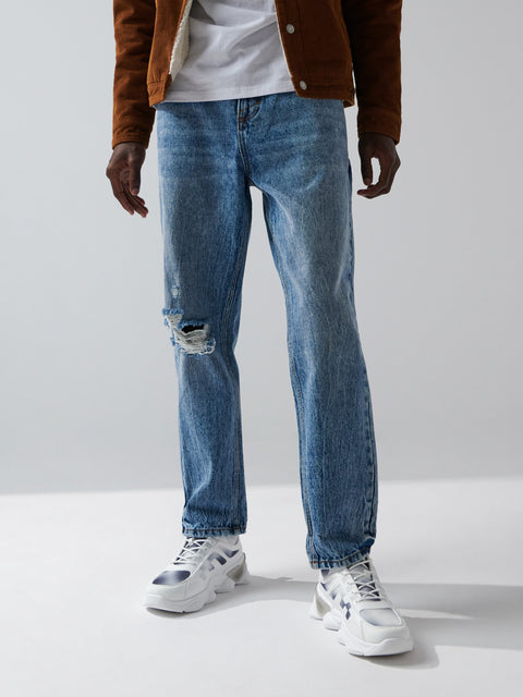 Person wearing blue jeans and a brown jacket on a plain background